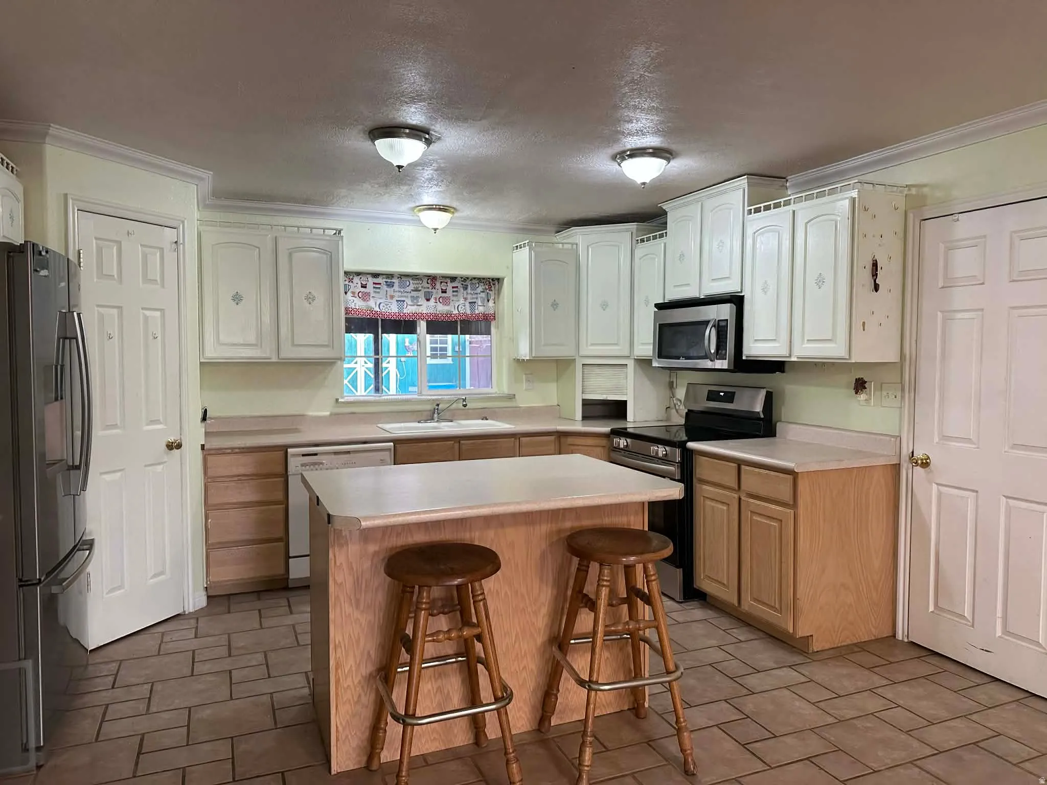 Kitchen with a breakfast bar, appliances with stainless steel finishes, a textured ceiling, light countertops, and ornamental molding
