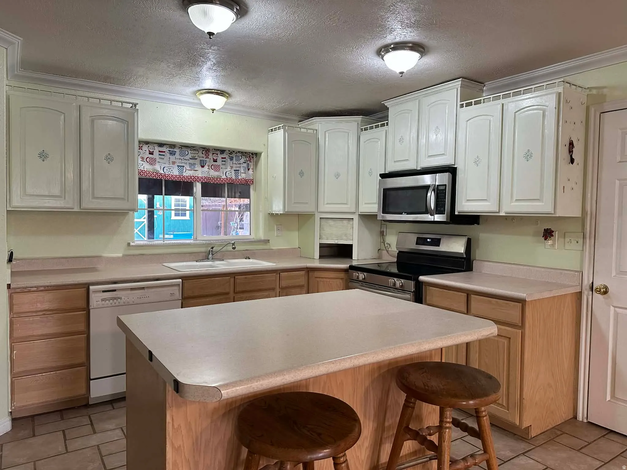 Kitchen featuring a kitchen bar, a textured ceiling, stainless steel appliances, light countertops, and crown molding