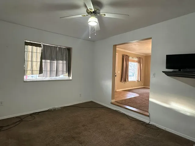 Spare room featuring dark colored carpet, a ceiling fan, and ornamental molding
