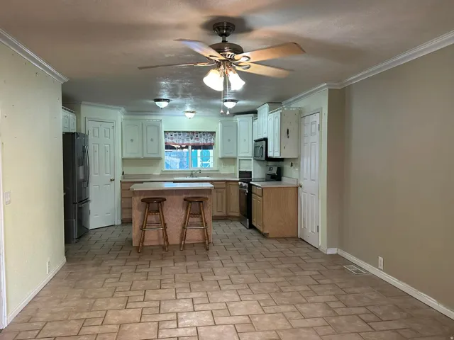 Kitchen with ceiling fan, electric range, light countertops, a kitchen breakfast bar, and stainless steel fridge