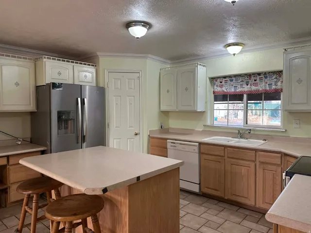 Kitchen with a textured ceiling, stainless steel fridge, a breakfast bar area, light countertops, and a kitchen island
