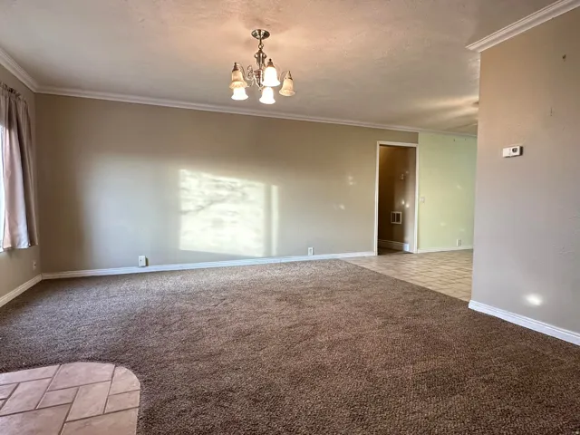 Spare room with light colored carpet, ornamental molding, a chandelier, and a textured ceiling