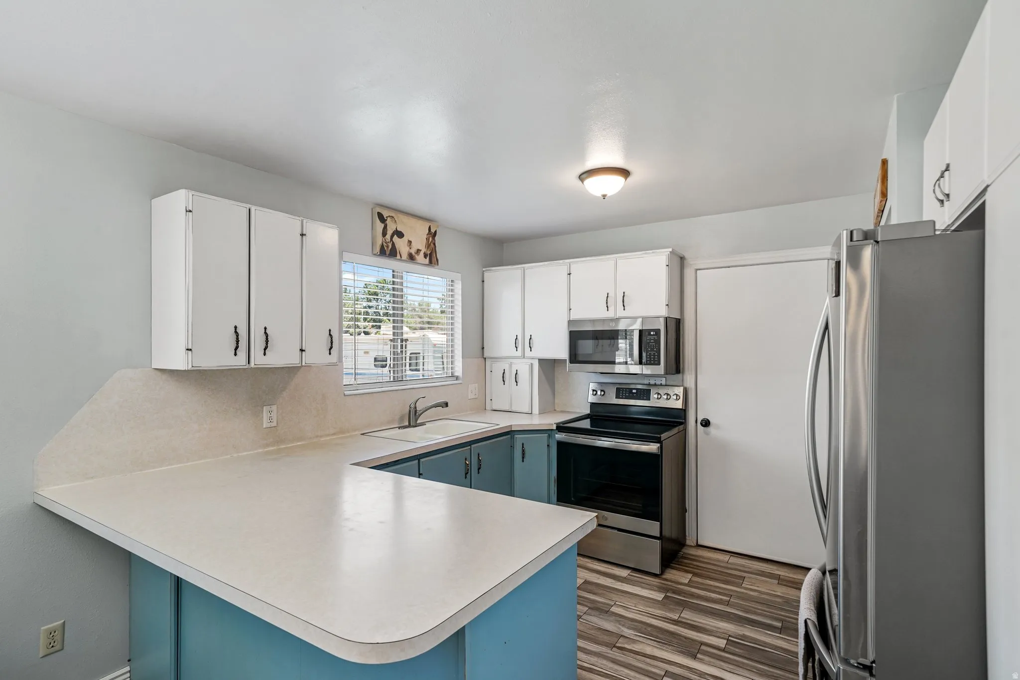 Kitchen featuring stainless steel appliances, a peninsula, light countertops, decorative backsplash, and white cabinetry