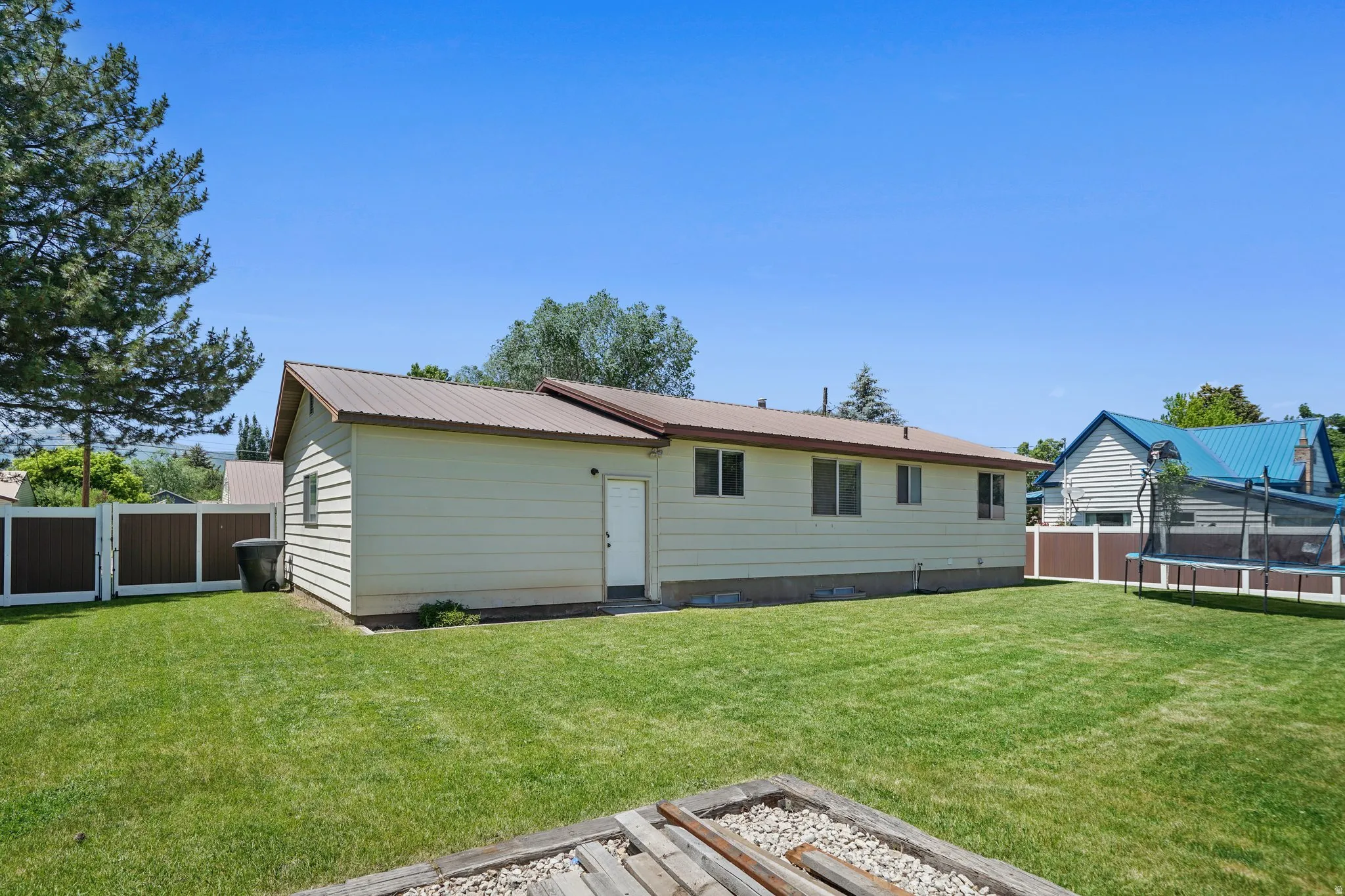 Rear view of house with a fenced backyard, a metal roof, a trampoline, and a gate