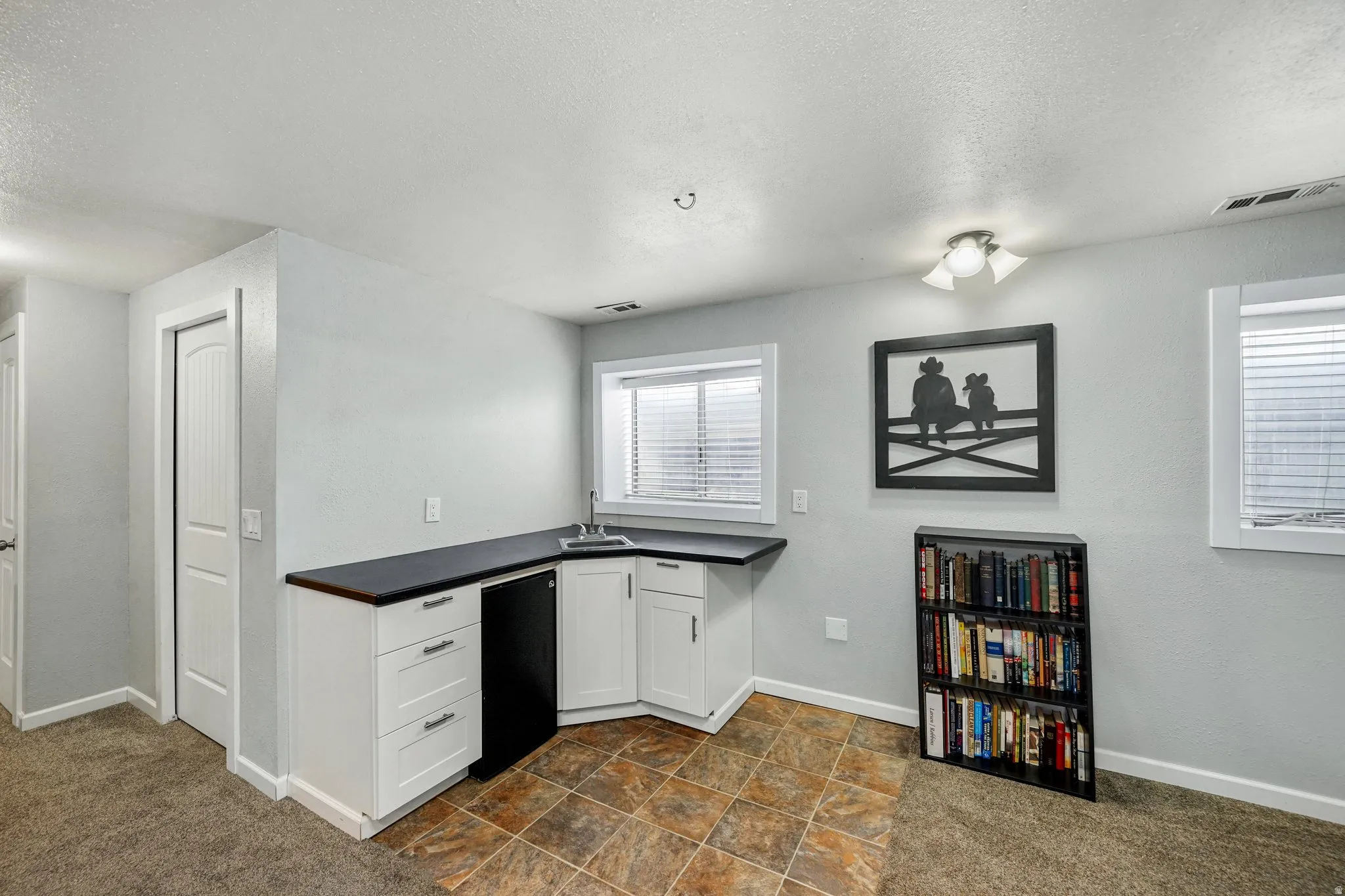 Kitchen with dark carpet, dark countertops, a textured ceiling, white cabinets, and stone finish flooring