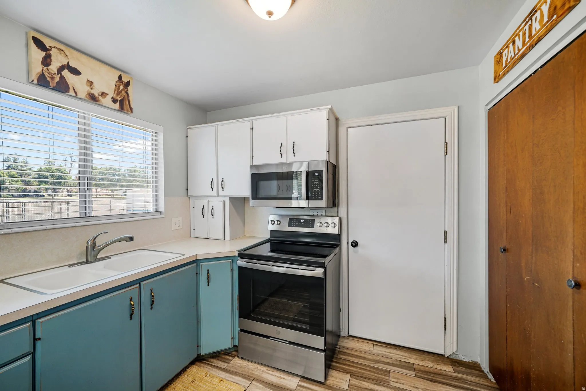 Kitchen with appliances with stainless steel finishes, light countertops, white cabinets, blue cabinetry, and light wood-style flooring