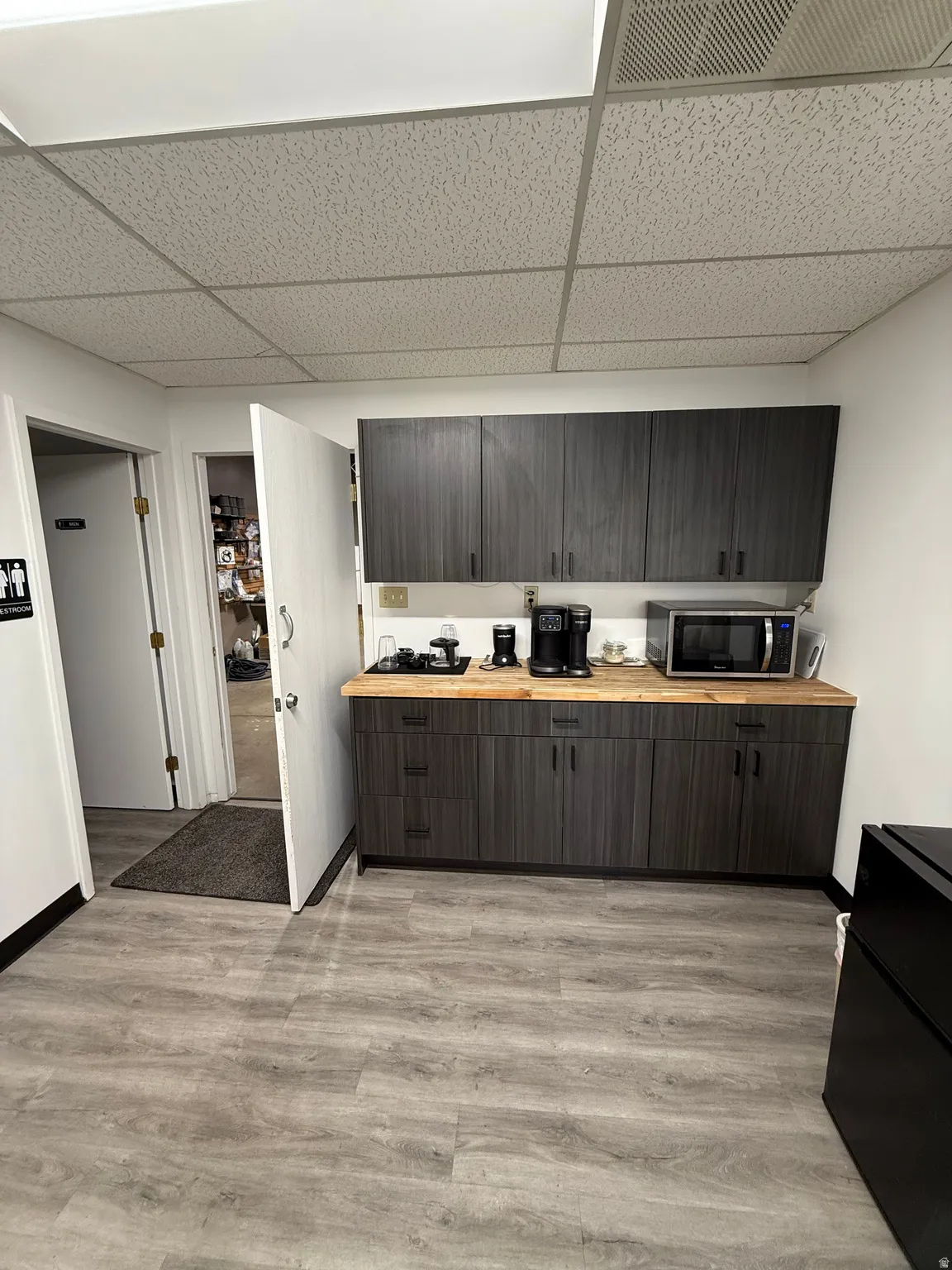 Kitchen with a drop ceiling, light wood finished floors, stainless steel microwave, butcher block counters, and dark brown cabinets
