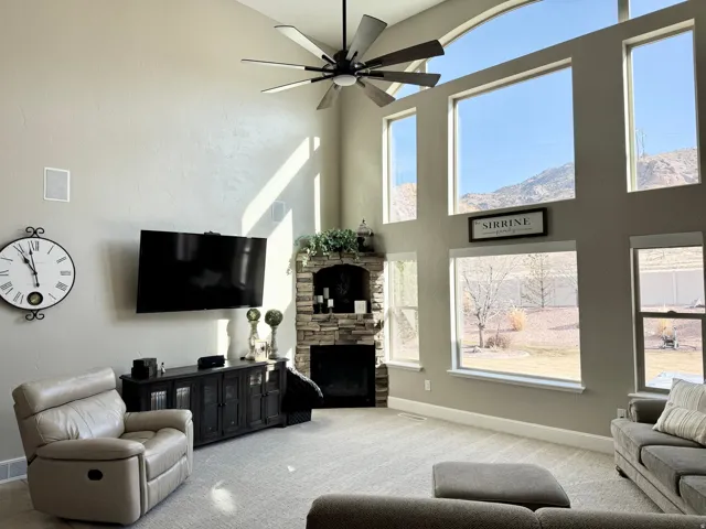 Living area featuring carpet flooring, a high ceiling, a ceiling fan, and a stone fireplace
