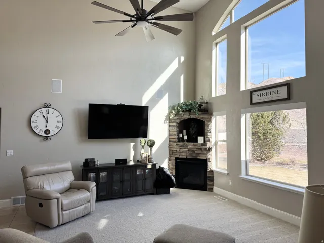 Carpeted living room with a ceiling fan, a stone fireplace, and a high ceiling