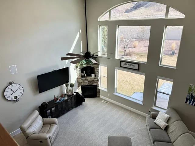 Living room with a towering ceiling, a fireplace, a ceiling fan, carpet, and plenty of natural light