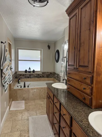 Full bathroom featuring stone tile floors, double vanity, a garden tub, and a textured ceiling