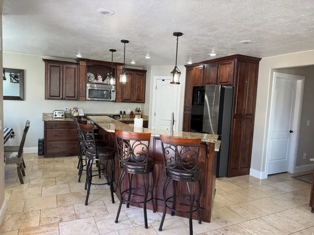Kitchen featuring a breakfast bar area, pendant lighting, light stone countertops, dark brown cabinets, and a textured ceiling