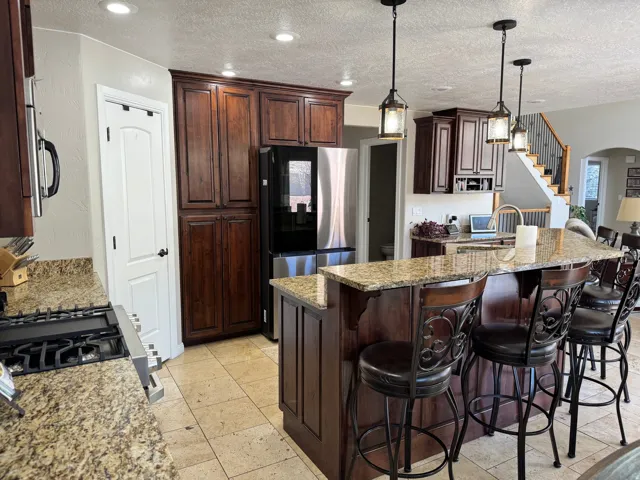 Kitchen featuring light stone counters, arched walkways, dark brown cabinets, stainless steel appliances, and a textured ceiling