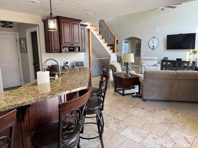 Kitchen featuring open floor plan, light stone counters, dark brown cabinets, a kitchen bar, and arched walkways