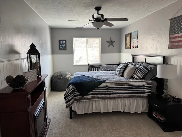 Bedroom with carpet, wainscoting, a textured ceiling, and ceiling fan