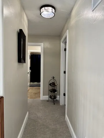 Hallway with a textured ceiling and light colored carpet