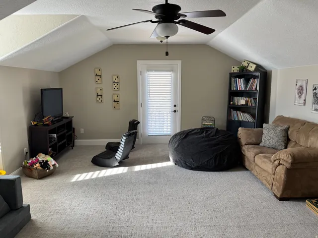Carpeted living area with a textured ceiling, lofted ceiling, and ceiling fan