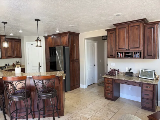 Kitchen featuring dark brown cabinets, light stone countertops, freestanding refrigerator, hanging light fixtures, and recessed lighting