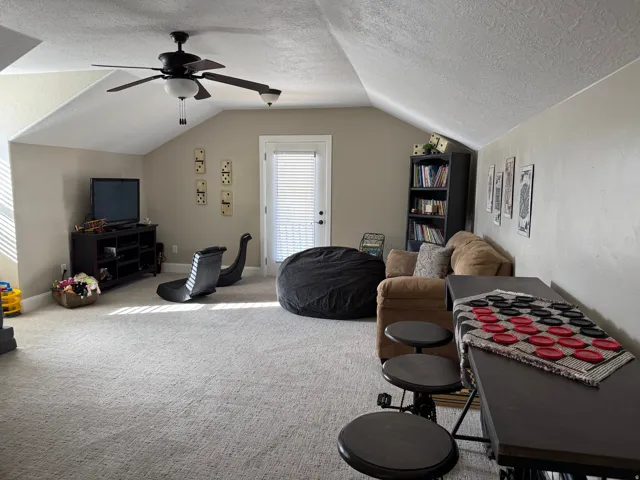 Carpeted living room with a textured ceiling, lofted ceiling, and a ceiling fan
