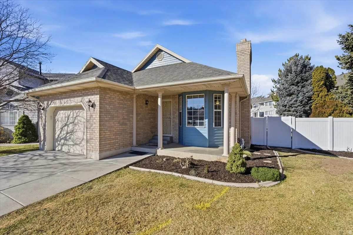 Ranch-style home with a porch, brick siding, an attached garage, a gate, and a chimney