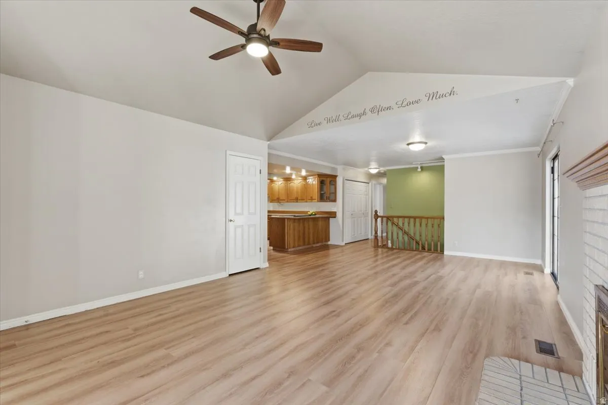 Unfurnished living room with vaulted ceiling, light wood-type flooring, a ceiling fan, and crown molding