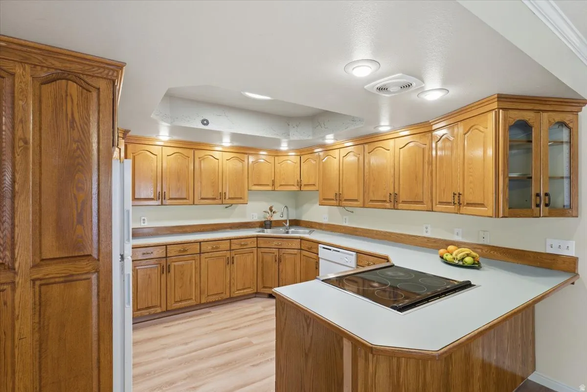Kitchen featuring light countertops, brown cabinets, white appliances, and light wood-type flooring