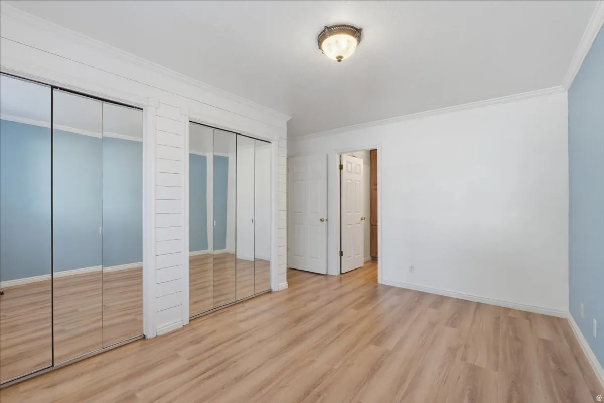 Unfurnished bedroom featuring two closets, wood finished floors, and ornamental molding