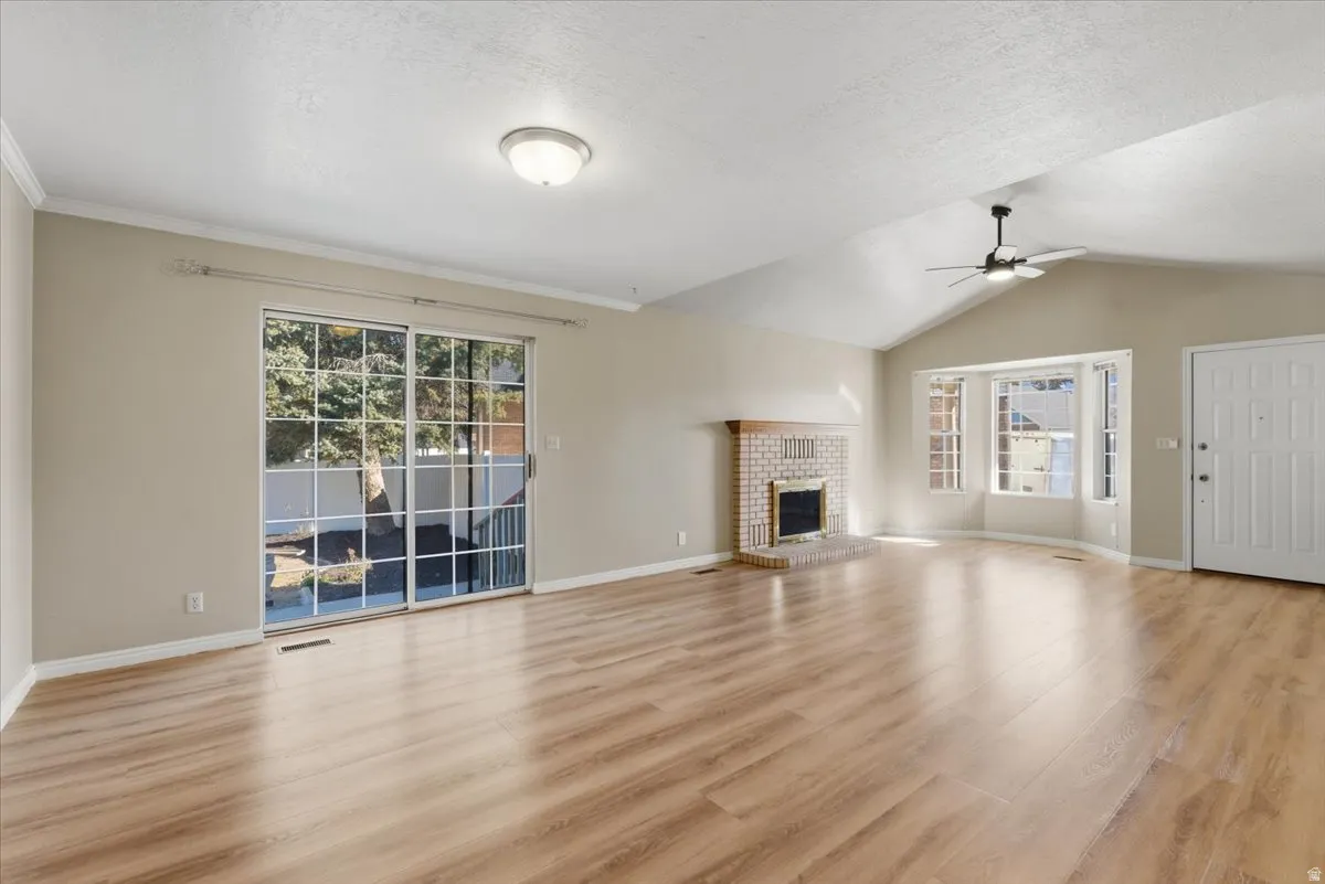 Unfurnished living room featuring a brick fireplace, light wood-style flooring, a ceiling fan, lofted ceiling, and a textured ceiling