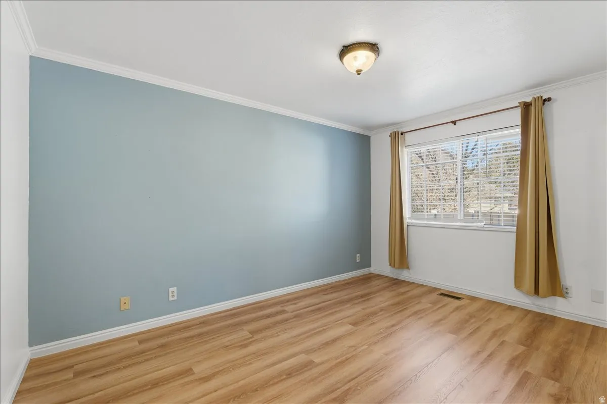 Unfurnished room with crown molding and light wood-type flooring
