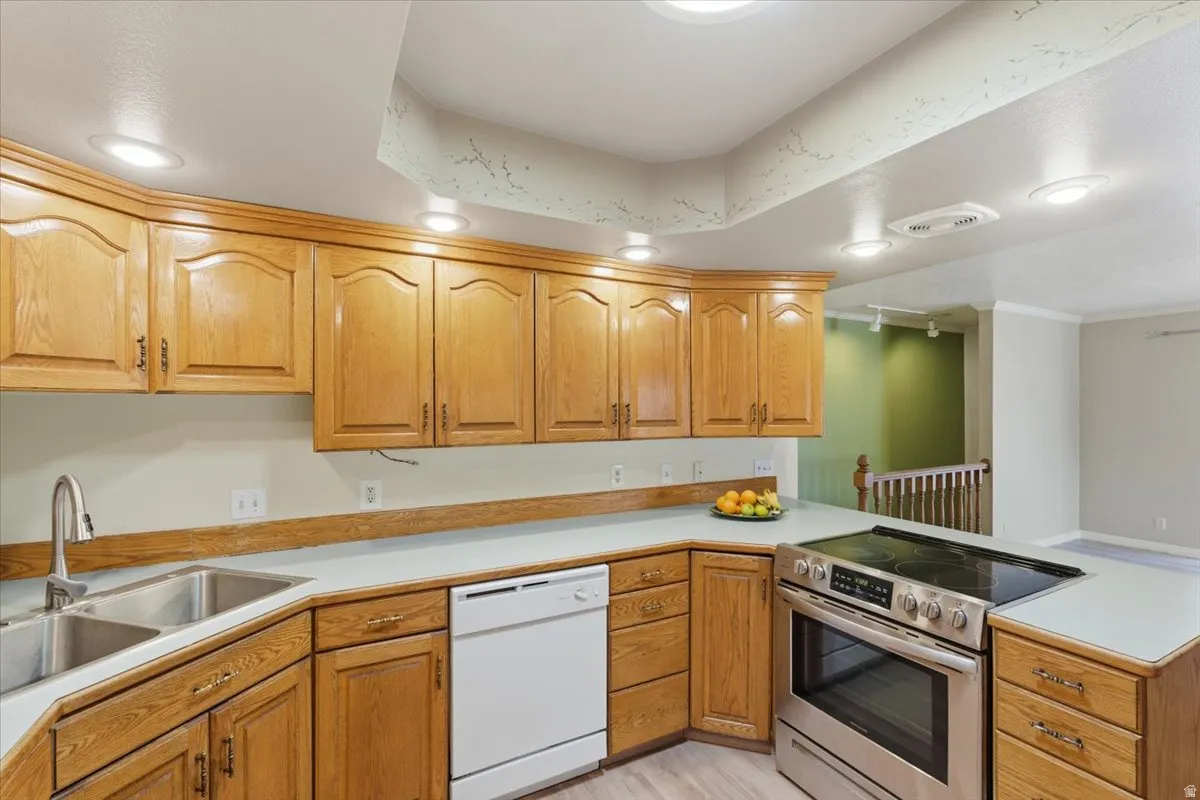 Kitchen featuring stainless steel electric range, light countertops, dishwasher, a peninsula, and brown cabinets
