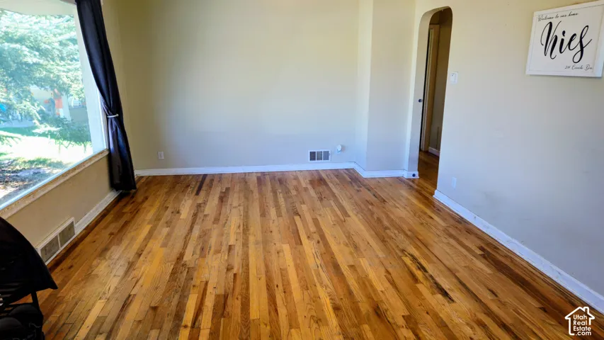 Hardwood flooring, arched doorway, large window, and light-toned walls
