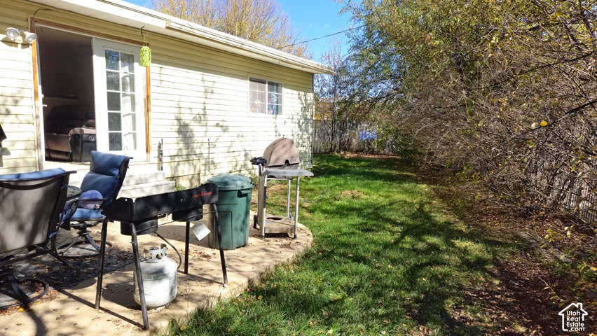 Exterior featuring light-colored horizontal siding, concrete slab patio, and rear lawn bordered by mature trees
