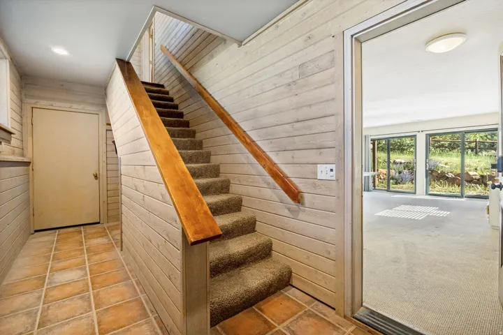 Carpeted staircase with a wood handrail, set against horizontal wood-finish paneling