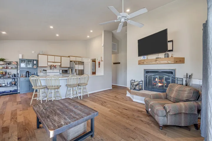 Living room with light wood finished floors, high vaulted ceiling, a glass covered fireplace, a ceiling fan, and recessed lighting