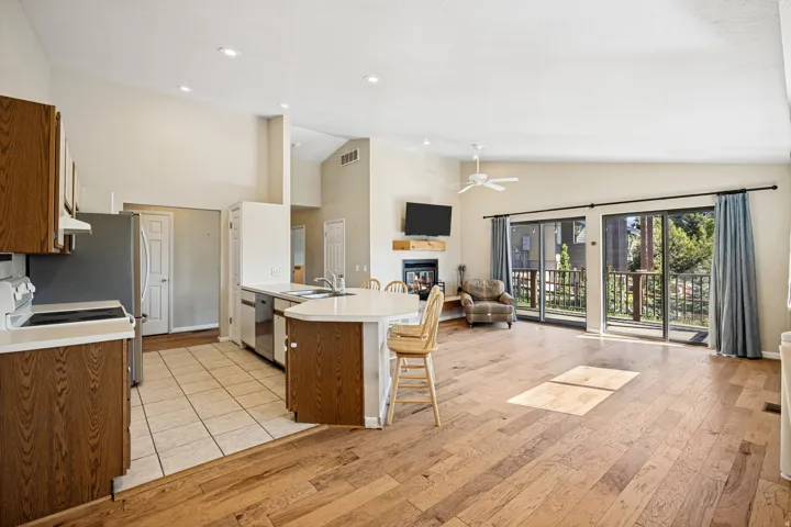 Open-concept living area featuring vaulted ceilings, wood-finish flooring, a contemporary fireplace, and sliding glass doors opening to an outdoor space