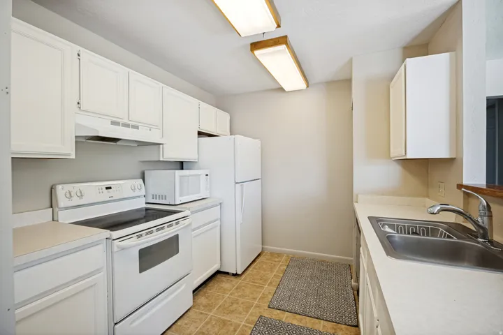 Kitchen featuring white cabinetry, white appliances, light countertops, and tile flooring