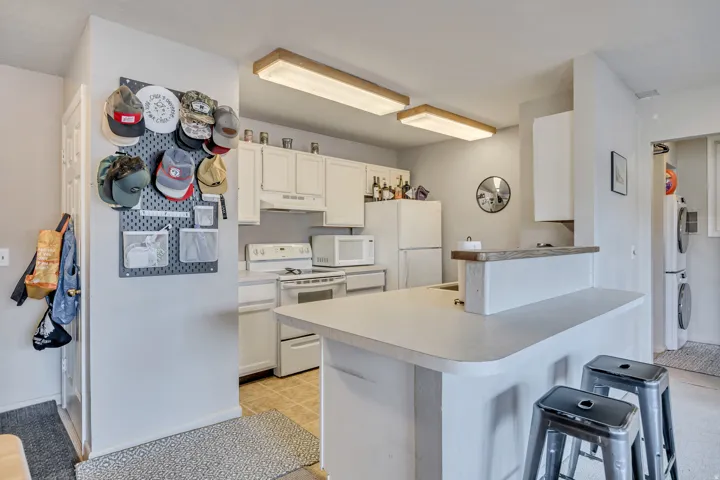 Kitchen with white cabinetry, white appliances, a kitchen bar, a peninsula, and light countertops