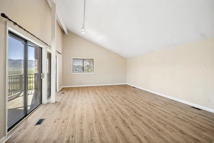 Spacious room featuring wood-finish flooring, vaulted ceilings, and a large picture window
