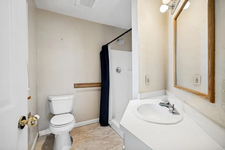 Compact bathroom featuring a shower stall, single vanity with integrated sink, wood-finish framed mirror, and tile flooring