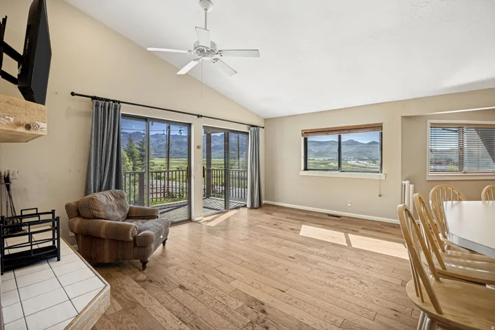Vaulted ceiling living area featuring wood-finish flooring, a white ceiling fan, and a fireplace with a wood mantel
