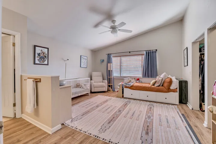 Bedroom featuring vaulted ceiling, light wood-style flooring, ceiling fan, and a crib