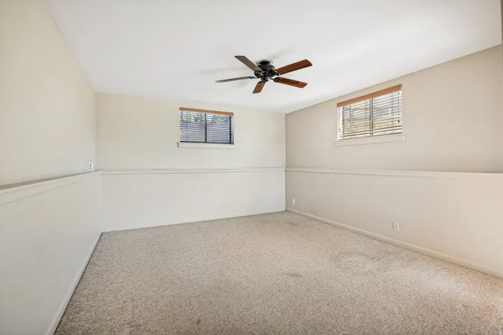 Spacious room featuring neutral carpeting, light-toned walls, and a ceiling fan