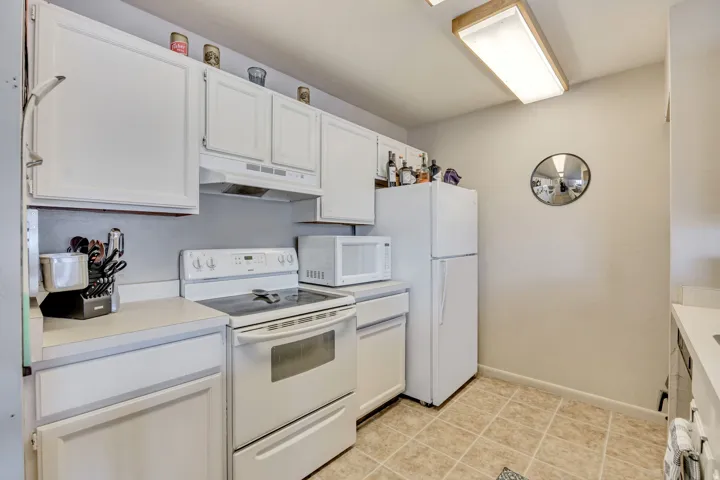 Kitchen with white appliances, light countertops, white cabinets, and under cabinet range hood