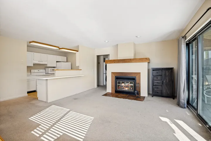 Open-concept living area featuring a fireplace with a wood mantel and tile surround, white kitchen cabinetry, a kitchen peninsula, and sliding glass doors
