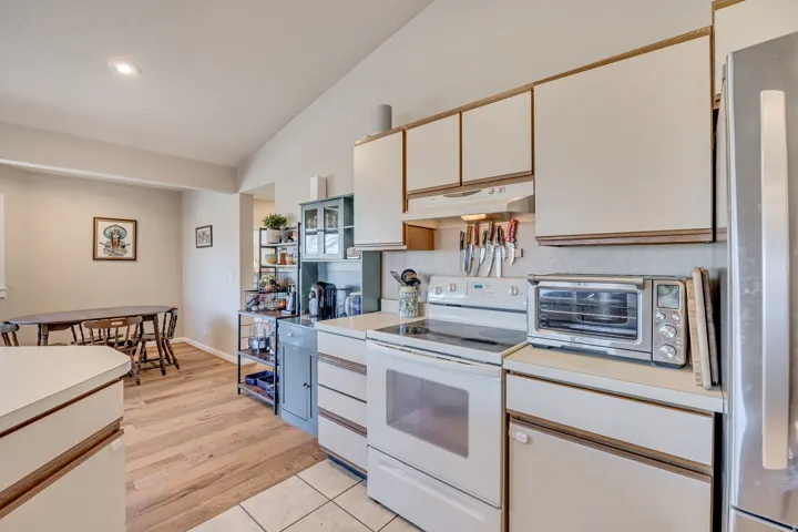 Kitchen featuring white electric stove, lofted ceiling, open shelves, light countertops, and freestanding refrigerator