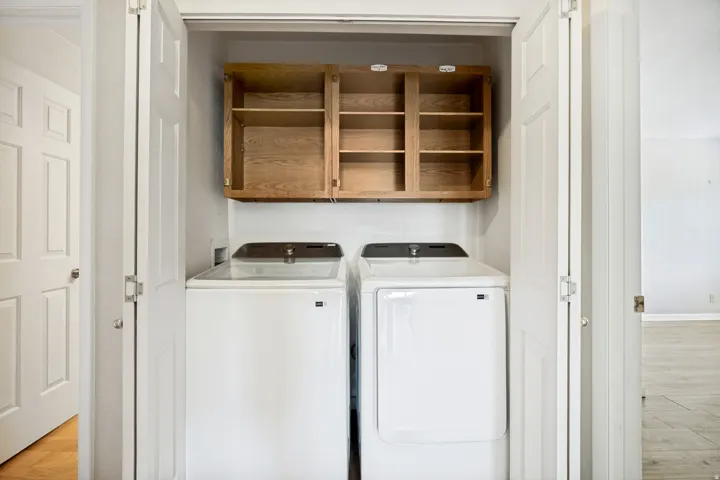 Built-in laundry closet featuring wood-finish cabinetry, white bi-fold doors, and a light-colored wall finish