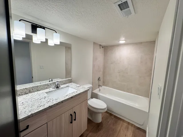 Bathroom featuring a textured ceiling, vanity, tub / shower combination, and dark wood-style flooring