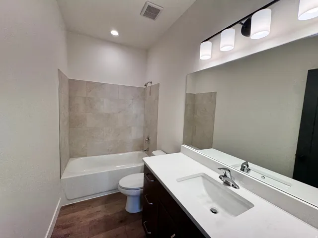 Full bath featuring washtub / shower combination, vanity, and dark wood-type flooring