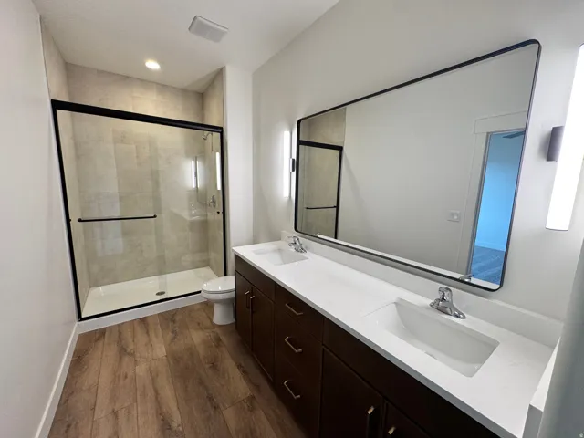 Bathroom featuring double vanity, dark wood finished floors, a shower stall, and recessed lighting