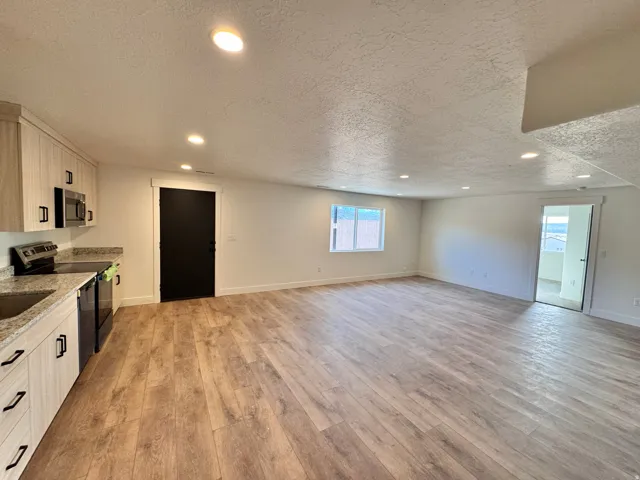 Kitchen featuring recessed lighting, stainless steel appliances, light wood-style floors, a textured ceiling, and light stone countertops